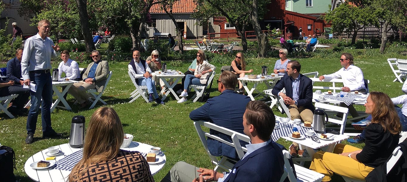 Utomhusnätverk på en gräsmatta med kaffe, kaka och röda trähus i bakgrunden
